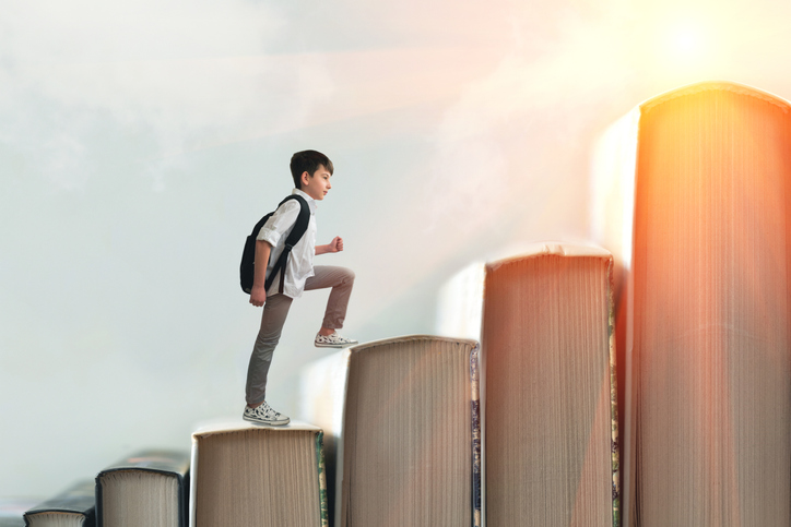 Child climbing stairs made of on sky background. Education or hard study concept. Soft focus
